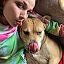 person, dog, couch, purple_hair, tongue_out, tan_dog, casual_clothing, tie_dye_sweatshirt, relaxed, indoor, pet, companion, tongue, nose, blanket, resting, close_up, playful, friendship, home