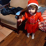 Justine a rejoint le concours — aidez-le/la à gagner de superbes lots ! toddler, child, red_dress, santa_hat, indoor, wooden_floor, chair, furniture, motion_blur, person, holiday_outfit, socks, cabinet, cushion, striped_pillow, home, brown_hair, young_child, floor_tiles, cozy