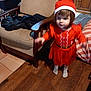 toddler, child, red_dress, santa_hat, indoor, wooden_floor, chair, furniture, motion_blur, person, holiday_outfit, socks, cabinet, cushion, striped_pillow, home, brown_hair, young_child, floor_tiles, cozy