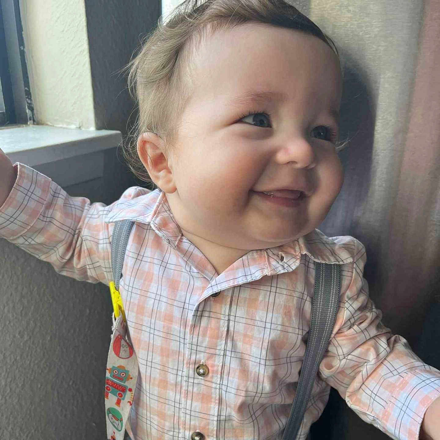Oliver is registered to the contest to win money with this photo: baby, baby_boy, buttoned_shirt, cheeks, child, clothing, cute, expression, face, hair, happy, indoors, natural_light, person, plaid_shirt, portrait, smile, standing, suspenders, window