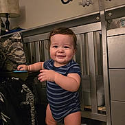 Oliver is registered to the contest to win money with this photo: toddler, baby, crib, nursery, smiling, drool, blue_onesie, carpet, lamp, blanket, furniture, child, standing, indoor, home, toy, pillow, decor, person, room