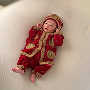 Kungahang is registered to the contest to win money with this photo: baby, infant, clothing, red, gold, embroidery, hat, lying_down, texture, fabric, cute, portrait, child, small, soft, looking_up, hands_up, barefoot, indoors, light