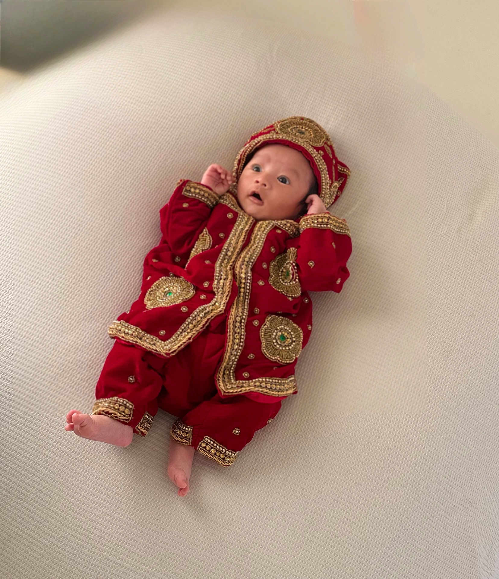 Kungahang is registered to the contest to win money with this photo: baby, infant, clothing, red, gold, embroidery, hat, lying_down, texture, fabric, cute, portrait, child, small, soft, looking_up, hands_up, barefoot, indoors, light