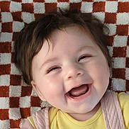 Mia joined the competition — help win amazing prizes! baby, blanket, checkered_pattern, cheerful, child, closeup, cute, expression, face, happy, indoor, infant, lying_down, pink_overalls, portrait, smiling, soft_lighting, wooden_button, yellow_clothing, young_child