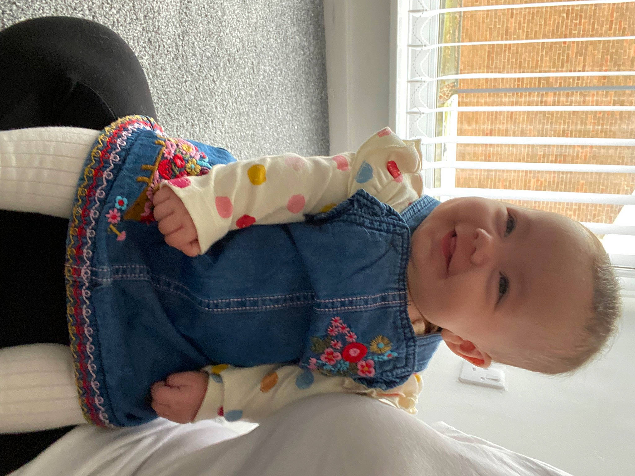 Lillie is registered to the contest to win money with this photo: arm, baby, baby_toddler_clothing, child, comfort, couch, dress, finger, human_body, human_leg, joint, joy, leg, linens, pattern, person, room, sitting, sleeve, textile