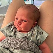 Artie is registered to the contest to win money with this photo: newborn, baby, blanket, clothing, mickey_mouse, person, infant, skin, head, face, sitting, indoors, lap, soft_texture, cute, child, young, comfort, rest, portrait