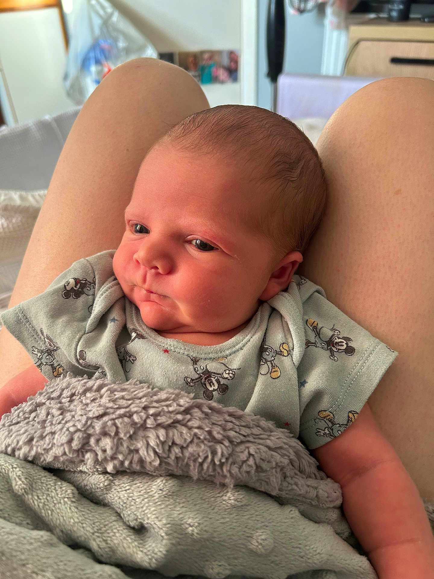 Artie is registered to the contest to win money with this photo: newborn, baby, blanket, clothing, mickey_mouse, person, infant, skin, head, face, sitting, indoors, lap, soft_texture, cute, child, young, comfort, rest, portrait