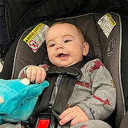 Kingston is registered to the contest to win money with this photo: baby, car_seat, child, smiling, plush_toy, clothing, straps, safety, face, infant, cute, happy, indoors, seat_belt, hands, head, person, cozy, fabric, closeup