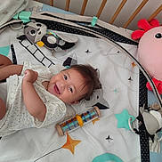 Raphaëlle a rejoint le concours — aidez-le/la à gagner de superbes lots ! baby, crib, toy, smile, happy, infant, playmat, stuffed_animal, colorful, soft_toys, child, cute, lying_down, indoors, baby_clothes, head, face, expression, joy, background