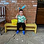 Brayden is registered to the contest to win money with this photo: toddler, child, bench, yellow_bucket, bunny_ears, dinosaur_shirt, blue_shoes, brick_wall, chalk_drawings, sidewalk, outdoor, concrete, playful, cute, smiling, person, casual_clothing, daylight, wooden_chair, yellow_bench