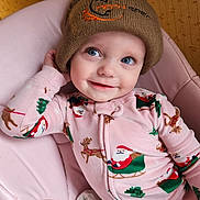 Octavia joined the competition — help win amazing prizes! baby, infant, child, beanie, hat, blue_eyes, smile, onesie, santa_print, reindeer_pattern, pink_chair, pajamas, portrait, cute, holiday_theme, looking_up, hand_on_head, indoor, soft_lighting, cozy