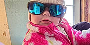 Octavia is registered to the contest to win money with this photo: baby, infant, child, sunglasses, knit_hat, pink_fur_jacket, fuzzy_coat, door, window, indoor, hand, portrait, face, chubby_cheeks, reflection, winter_clothing, cute, holding, person, home_interior