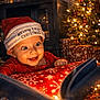 baby, celebration, christmas, christmas_tree, cozy, cute, decorations, face, festive, glowing_book, happy, holiday, indoors, infant, joy, presents, red_clothing, santa_hat, smiling, warm_lighting