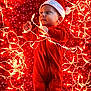baby, blanket, celebration, child, christmas, christmas_lights, curious, cute, festive, holiday, indoors, infant, lying_down, portrait, red_onesie, santa_hat, snowflake_pattern, string_lights, tangled, warm_lighting