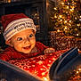 baby, book, child, christmas, cozy, decorations, face, festive, happy, hat, holiday, indoors, joy, lights, present, red_clothing, smile, tree, warm_lighting, wrapped_gifts