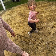 Bria is registered to the contest to win money with this photo: child, toddler, pink_clothing, black_leggings, sandy_ground, outdoor, person, footwear, crocs, leash, curly_hair, motion, playful, expression, green_leash, casual, nature, grass, vehicle, background