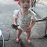 toddler, child, barefoot, onesie, toy, outdoor, patio, curious, standing, wide_eyes, ruffled_sleeves, blurry_background, hair, expression, footwear_none, concrete_floor, furniture, sunlight, person, young