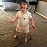 Bria is registered to the contest to win money with this photo: barefoot, baseball_cap, bedroom, cap, carpet, child, cute, floor, flower_embroidery, furniture, happy, home, indoor, person, pink_shorts, smiling, standing, toddler, white_shirt, young_child