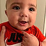 baby, close_up, face, hand, orange_shirt, smile, pointing, person, child, cute, portrait, indoor, skin, eyes, expression, clothing, adult_hand, wristband, happy, infant