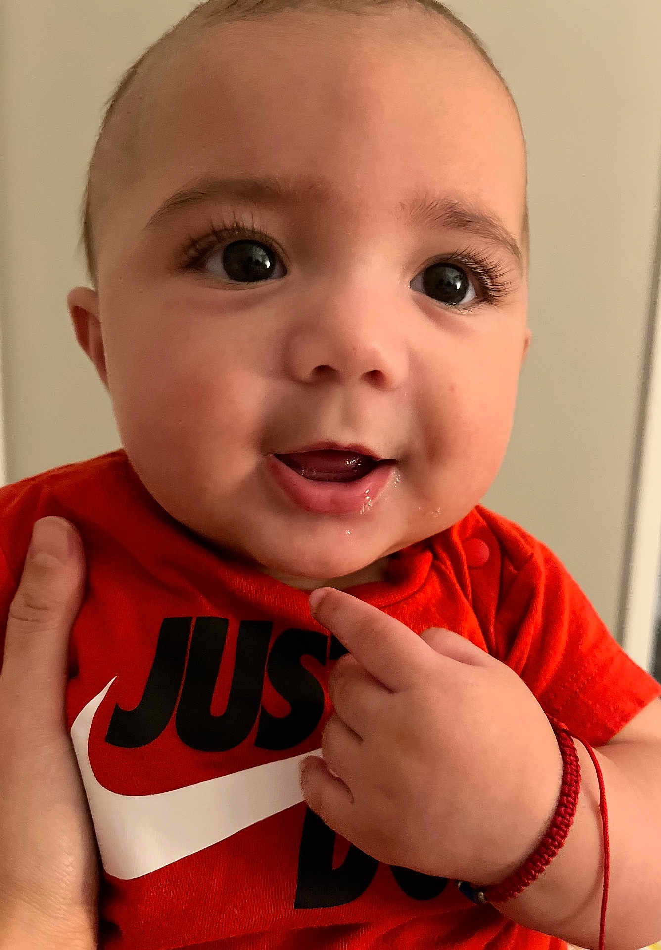Bradley joined the competition — help win amazing prizes! baby, close_up, face, hand, orange_shirt, smile, pointing, person, child, cute, portrait, indoor, skin, eyes, expression, clothing, adult_hand, wristband, happy, infant