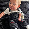 toddler, baby, child, overalls, white_tshirt, couch, black_couch, baby_bottle, sitting, indoors, light_hair, ripped_jeans, smiling, cute, portrait, face, happy, cozy, furniture, casual_clothing