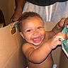 baby, child, cardboard_box, diaper, smiling, happy, playing, indoor, person, adult_hand, cute, joyful, expression, young_child, fun, family, home, holding, sitting, face