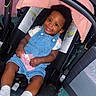 toddler, child, car_seat, denim_overalls, socks, indoor, smiling, baby, happy, seatbelt, pink_cloth, floor, furniture, head_support, curly_hair, playpen, cushion, clothing, person, portrait