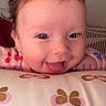 baby, child, smiling, tongue_out, blue_eyes, face, pillow, butterfly_pattern, indoor, closeup, cute, happy, infant, pink_clothing, patterned_fabric, portrait, young_child, cheerful, head, playful