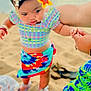 adult_hand, baby_shoes, beach, child, colorful_clothing, flower_clip, footwear, hand_holding, necklace, ocean, outdoor, patterned_skirt, person, playful, sand, short_sleeve_top, summer, sunset, toddler, vacation