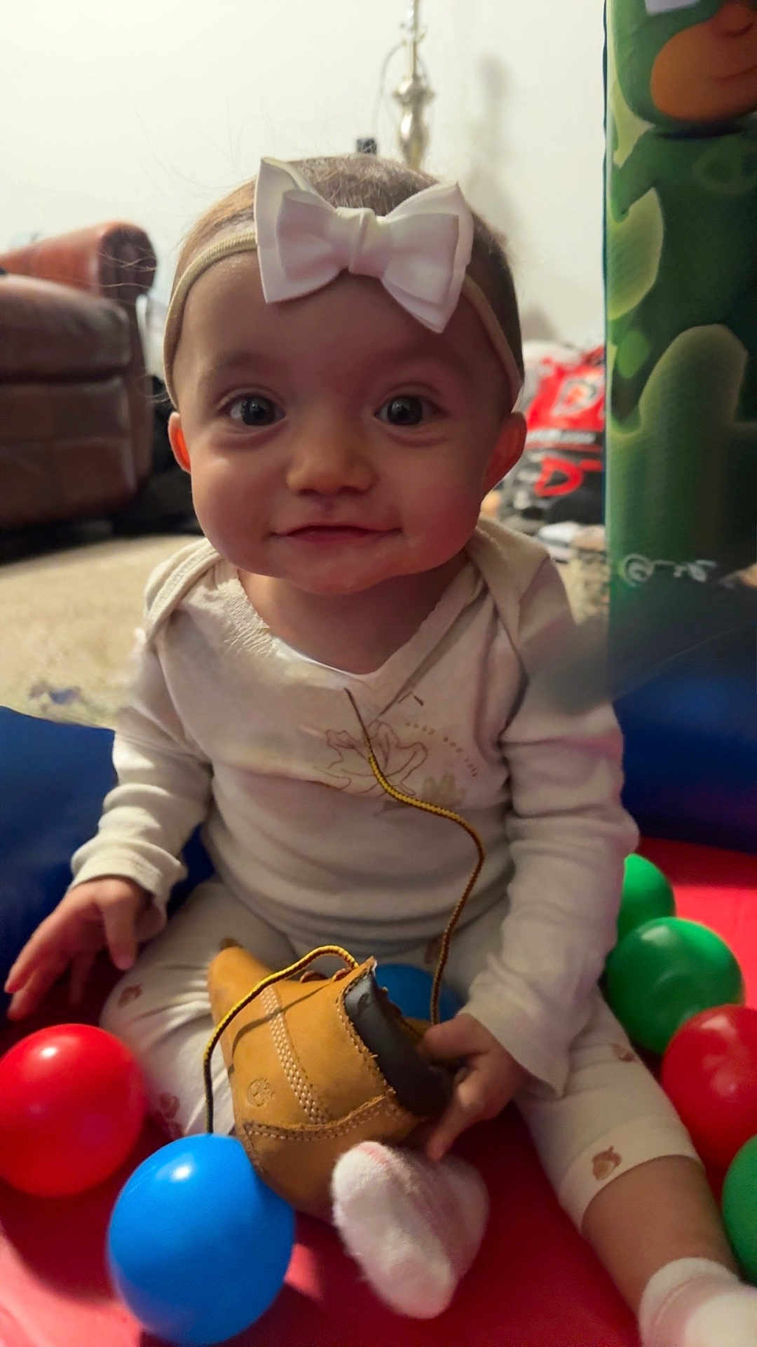 Imoni joined the competition — help win amazing prizes! baby, child, headband, bow, toy, shoe, boot, colorful_balls, sitting, living_room, couch, carpet, infant, white_clothing, sock, cute, smiling, indoor, playtime, portrait