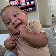 Joaquin joined the competition — help win amazing prizes! baby, infant, child, smiling, happy, face, portrait, sitting, indoors, bed, bedroom, television, home, clothing, onesie, hand, finger, chewing, family, close_up