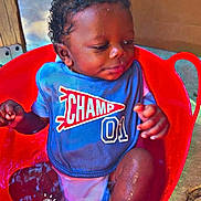 Jayden is registered to the contest to win money with this photo: baby, child, water, red_tub, bib, blue_clothing, outdoor, sitting, happy, cute, infant, foot, hand, wet, concrete, cardboard_box, relaxed, portrait, daylight, smile