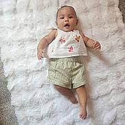 Florence is registered to the contest to win money with this photo: arms_outstretched, baby, barefoot, blanket, child, clothing, cute, face, floral_top, happy, indoor, infant, laying_down, person, portrait, smiling, soft_texture, striped_shorts, white_blanket, young_child