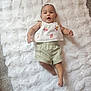 arms_outstretched, baby, barefoot, blanket, child, clothing, cute, face, floral_top, happy, indoor, infant, laying_down, person, portrait, smiling, soft_texture, striped_shorts, white_blanket, young_child