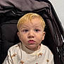 baby, blonde_hair, casual, child, clothing, cream_color, curious, cute, dog_print, expression, face, hazel_eyes, indoor, person, portrait, seated, shirt, stroller, toddler, young_child