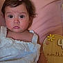 Carina is registered to the contest to win money with this photo: baby, infant, child, girl, pink_bow, white_dress, sitting, cushion, soft_toy, wooden_sign, months, portrait, cute, indoors, closeup, face, expression, curly_hair, skin, young
