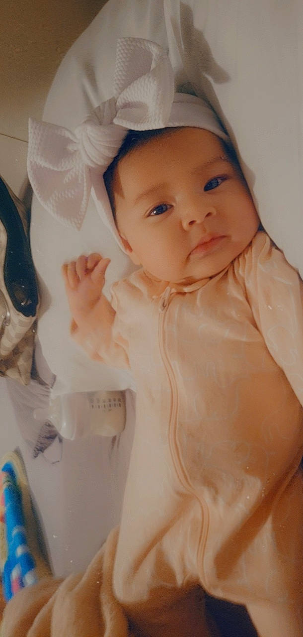 Amelie is registered to the contest to win money with this photo: arm, baby, baby_toddler_clothing, cheek, eye, eyebrow, eyelash, finger, hand, headwear, human_body, iris, lip, neck, nose, person, pink, skin, sleeve, stomach