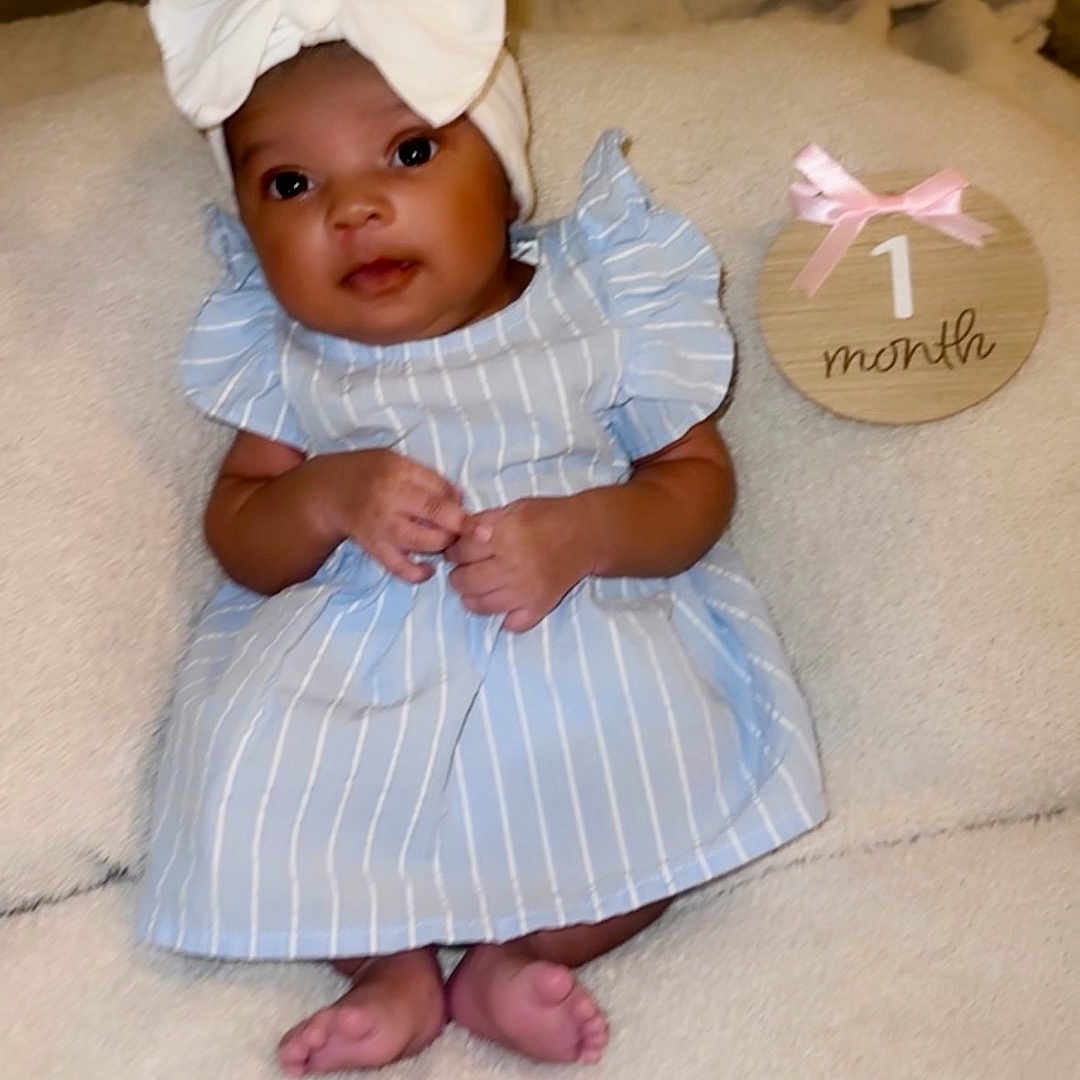 Aryana joined the competition — help win amazing prizes! baby, blanket, blue_dress, child, closeup, cute, feet, hands, headband, indoors, infant, lying_down, milestone, newborn, person, pink_ribbon, portrait, soft_texture, white_bow, wooden_sign