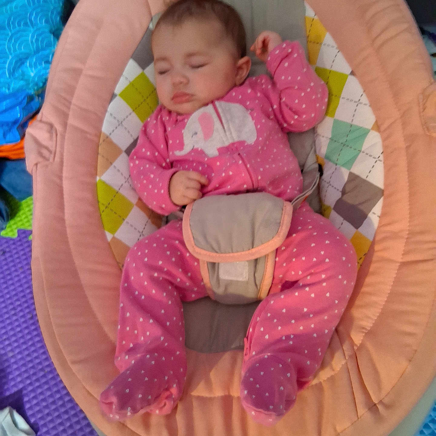 Elie is registered to the contest to win money with this photo: baby, baby_gear, baby_rocker, child, colorful_padding, cozy, cute, elephant_design, face, footed_pajamas, indoors, infant, onesie, peaceful, person, pink_clothing, play_mat, resting, sleeping, soft_toys