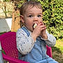child, toddler, girl, eating, snack, hands, face, eyes, hair_clip, plastic_chair, denim_dress, overalls, outdoor, garden, trees, portrait, sitting, pink, cute, food