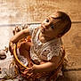 baby, child, wicker_basket, white_lace, curious, wooden_floor, indoors, soft_light, cute, portrait, hands, feet, sitting, young_child, closeup, natural_light, decor, floor, expression, infant