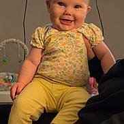 Havery Grace is registered to the contest to win money with this photo: baby, child, smiling, indoor, yellow_pants, floral_top, happy, person, face, cute, seated, toy, television, light, skin, hair, clothing, infant, cheerful, home