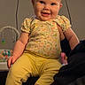 baby, child, smiling, indoor, yellow_pants, floral_top, happy, person, face, cute, seated, toy, television, light, skin, hair, clothing, infant, cheerful, home