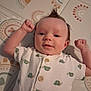 baby, child, clothing, cute, face, happy, head, indoor, infant, lying_down, mattress, mohawk_hairstyle, onesie, patterned_background, portrait, raised_fists, skin, smiling, turtle_pattern, young_child