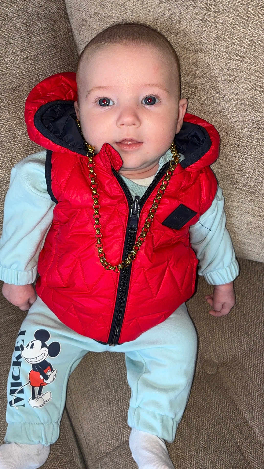 Kj Bourke joined the competition — help win amazing prizes! baby, child, red_vest, gold_chain, mickey_mouse, pants, socks, couch, seated, curious, indoor, face, blue_eyes, clothing, infant, portrait, cute, fashion, casual, comfort