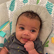 Truce is registered to the contest to win money with this photo: baby, infant, smiling, face, hand, curly_hair, onesie, blanket, seat, patterned_fabric, toucan, colorful, cute, comfort, child, portrait, happy, indoor, closeup, young