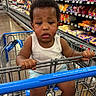 aisle, barefoot, child, clothing, floor, grocery_store, holding, indoor, metal_cart, packaged_goods, person, retail, serious_expression, shopping, shopping_cart, store, supermarket, tank_top, toddler, young_child