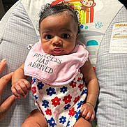 Nazari is registered to the contest to win money with this photo: baby, infant, child, onesie, bib, floral_pattern, hand_holding, baby_seat, sun_illustration, monkey_illustration, colorful, cute, portrait, indoors, person, skin, face, expression, curious, small_hand