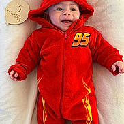 Layane participe au concours pour gagner de l'argent avec cette photo : baby, infant, red_onesie, hood, smiling, lying_down, blanket, milestone_sign, wooden_sign, face, expression, cute, child, baby_clothing, indoor, soft_texture, hand, eyes, headwear, car_design