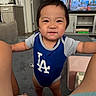 toddler, child, indoor, living_room, person, smiling, clothing, onesie, legs, furniture, television, carpet, cabinet, kitchen, floor, home, cute, baby, happy, portrait